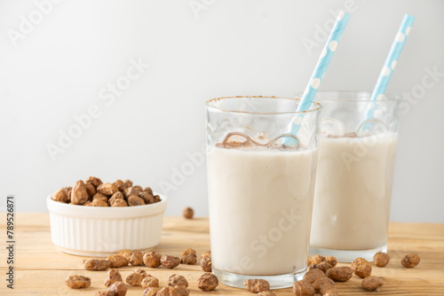 Close-up of two glasses with blue straws with horchata on table with tiger nuts, white background, horizontal, with copy space