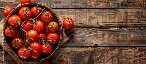 Top view of tomatoes in a bowl on the left side, against a wooden background with empty space for text. photo