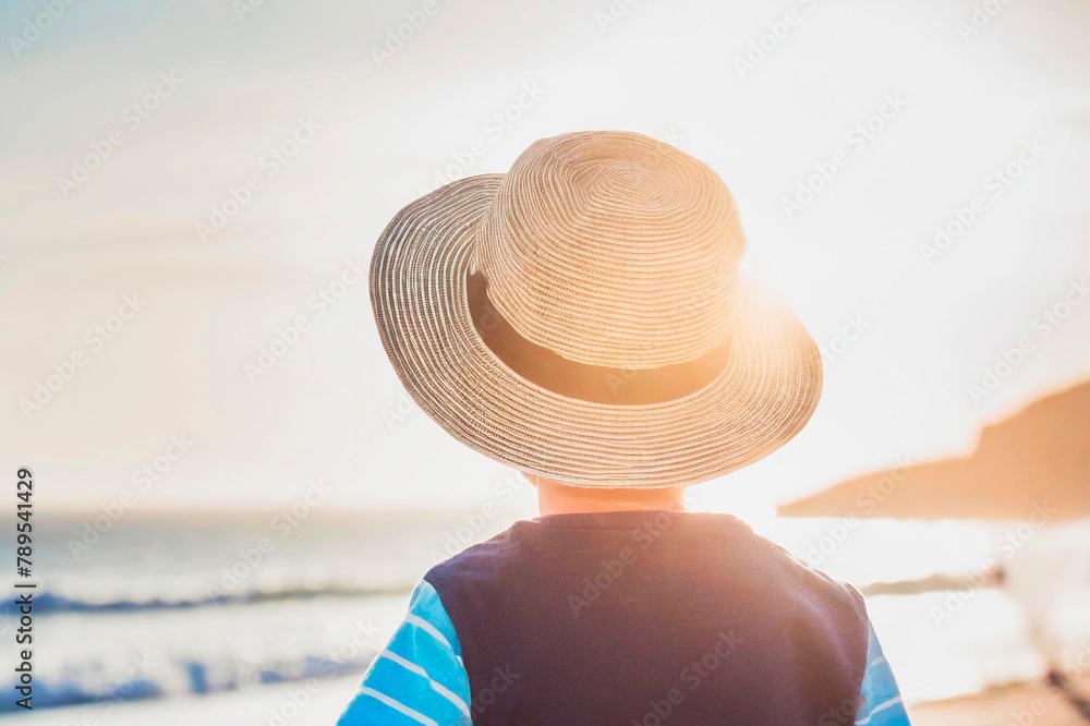 enfant de dos avec un chapeau de soleil, ambiance vacances - obrazy, fototapety, plakaty 