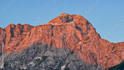 Panoramic sunrise view of mountain summit Mount Mangart in Julian Alps, Tarvisio, Friuli Venezia Giulia, Italy, Europe. Rock walls in warm red orange colors. Majestic landscape at alpine Lake Fusine photo