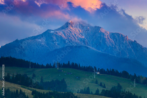 mountain sunset in the spring with Ceahlau peak in snow and green meadow on countryside of Romania Carpathians.