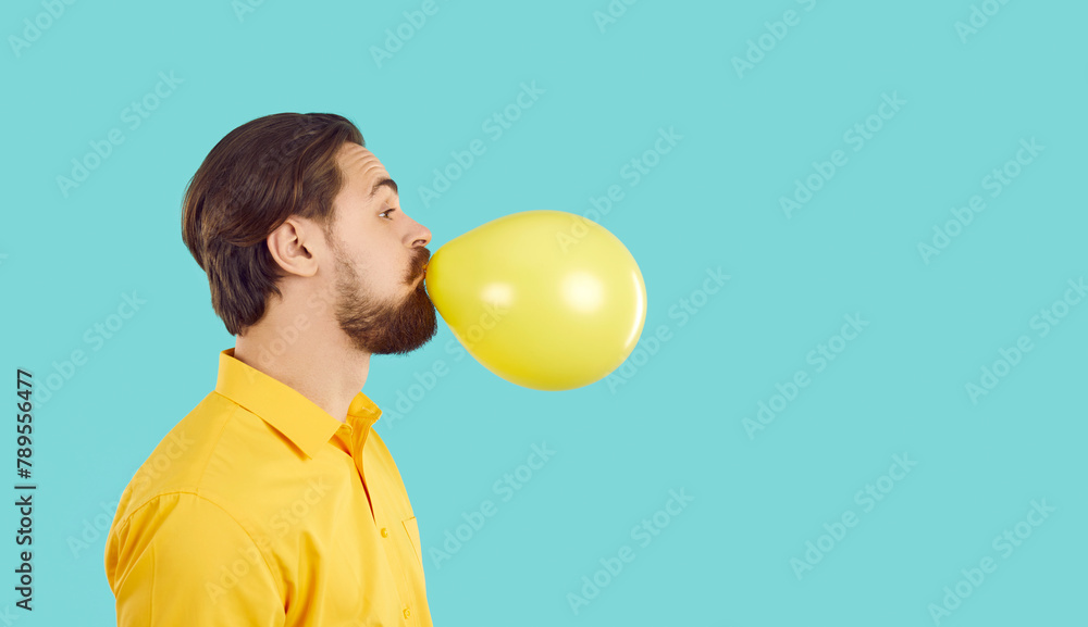 Young bearded man with funny expression inflates yellow ball on ...
