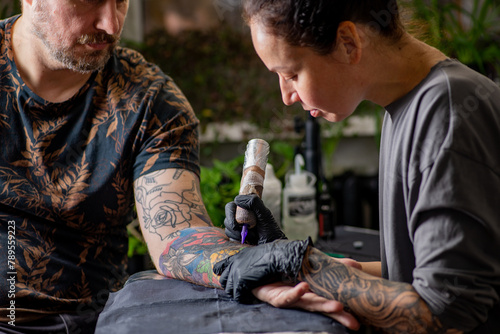 Woman tattoo artist tattooing man in salon photo
