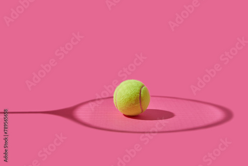 Yellow tennis ball placed among shadow in shape of racket photo