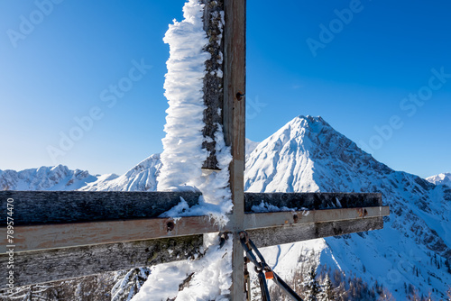 Scenic view of frozen summit cross Ferlacher Spitze in Karawanks, Carinthia, Austria. Clear blue sky in winter wonderland in remote Austrian Alps. Looking at snow capped mountain Mittagskogel (Kepa) photo