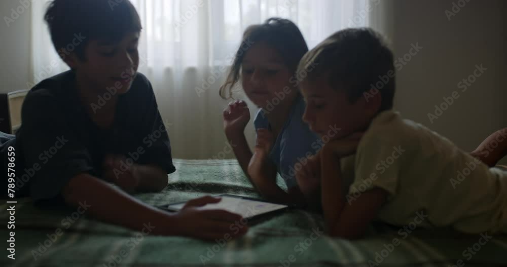 Three children engaged in playful interaction on a bed by a digital tablet at dusk Three children engaged in playful interaction on a bed by a digital tablet at dusk