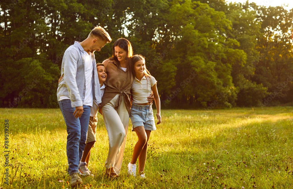 Happy smiling family of four with two kids boy and girl walking in summer park enjoying beautiful nature. Young joyful parents and their children hugging outdoors enjoying time together. Happy smiling family of four with two kids boy and girl walking in summer park enjoying beautiful nature. Young joyful parents and their children hugging outdoors enjoying time together.
