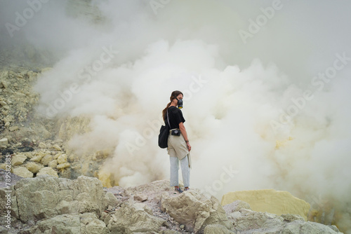 Traveller wearing respirator stands in volcano crater with sulfur gas photo