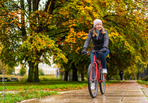 Mid-adult woman riding bicycle in city park on a rainy day
