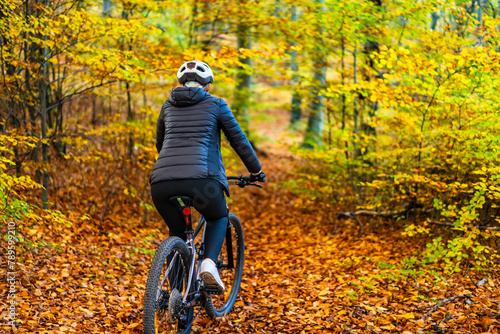 Woman riding bicycle in city forest in autumnal scenery
