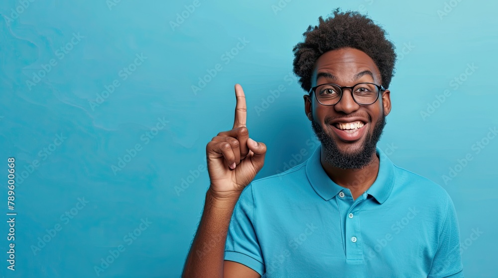 Portrait of smiling African American man, pointing finger up, has good idea genius plan, wearing a blue polo shirt. Portrait of smiling African American man, pointing finger up, has good idea genius plan, wearing a blue polo shirt.