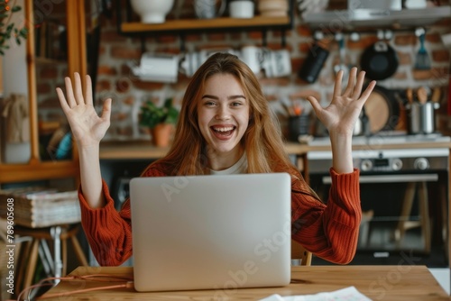 Portrait of a young happy female student sitting at home in the kitchen using a laptop and rejoicing at the good news. She looks at the camera, raised her hands in a victory, Generative AI