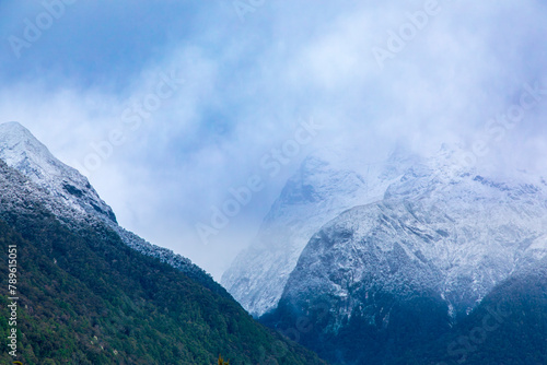 Photograph of cloud covered snow capped mountains with lush foliage in Fiordland National Park on the South Island of New Zealand