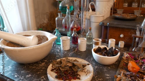 Chemistry flasks and beakers with colorful liquids, medicinal herbs and leaves of various plants, a mortar for grinding herbs, thermometer, butterfly wings and berries lie on table in an old pharmacy photo