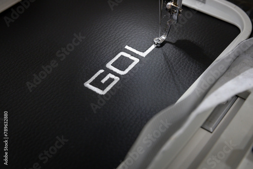 Machine embroidery of text with white thread on black leather. Embroidery on auto cushion.