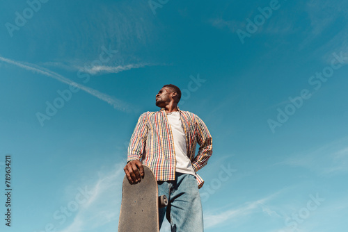 Black man with skateboard in blue sky with copyspace