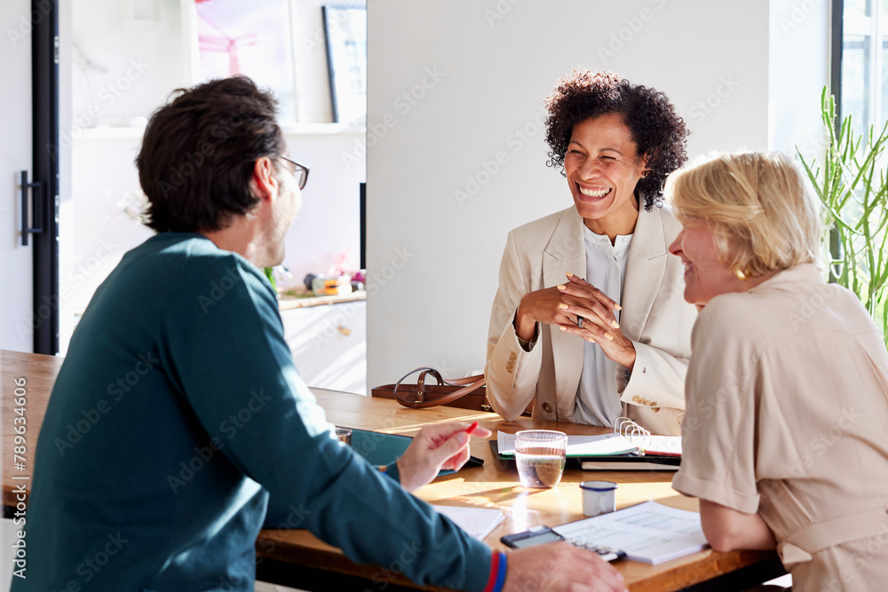 © ALTO IMAGES/Stocksy - Happy couple having finance discussion with consultant at home