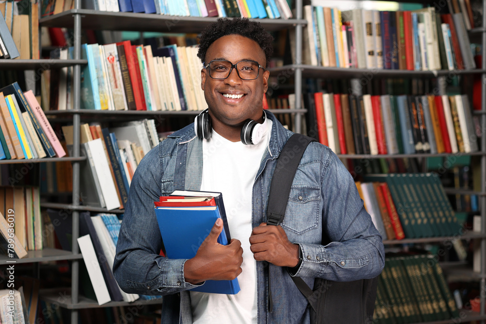 Happy male buyer chose interesting books in bookstore, happy with purchase. Portrait of smiling african college student with headphones around his neck, holding a stack of books. Happy male buyer chose interesting books in bookstore, happy with purchase. Portrait of smiling african college student with headphones around his neck, holding a stack of books.