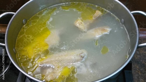 preparing delicious chicken broth in a silver pan in the home kitchen. an ingredient for further preparation of soup. light rich broth is good for the diet photo