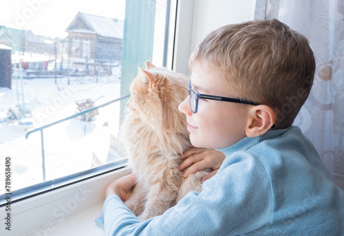 Obraz na płótnie Beautiful scene two friends looking out fo window. Small boy with a cat stares out of window watching falling snow, focus on cat w salonie