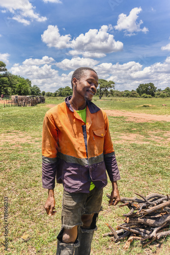 village young african man with a smile wearing orange workwear in the field selling wood