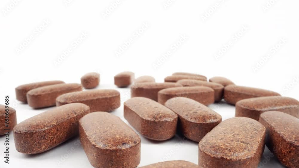 Array of brown herbal supplement tablets scattered on white surface Array of brown herbal supplement tablets scattered on white surface