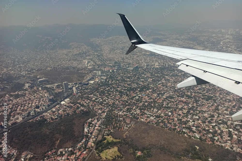 Fototapeta premium View through airplane window of commercial jet plane wing flying high in the sky ove big city. Air travelling concept