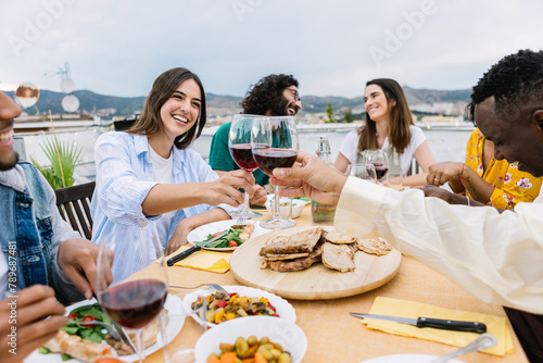 Happy group of friends enjoying dinner party on summer at home terrace. Food and summertime lifestyle concept