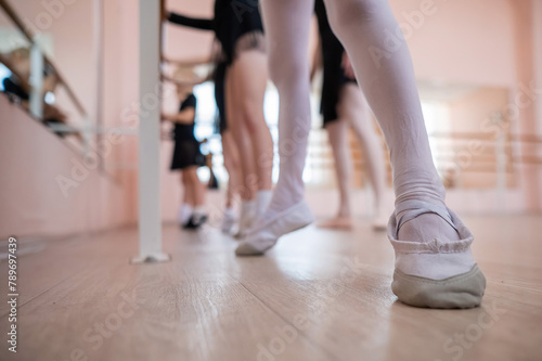 Little girls practice ballet at the barre. Close-up of young ballerinas' feet. 