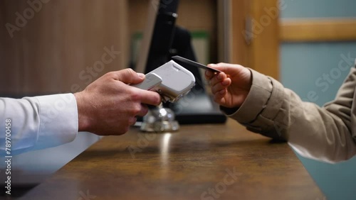 Woman making payment with credit card, receptionist holding credit card reader in hotel