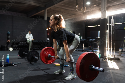 Woman lifting a barbell with weights in the gym at sunset. photo
