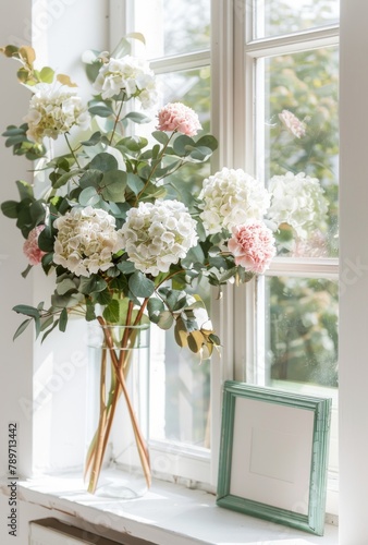 Pink and white hydrangeas in a  vase on table  a small green picture mockup frame  against the window 