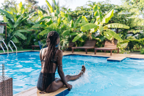 Faceless young black woman sitting at poolside with blue water photo
