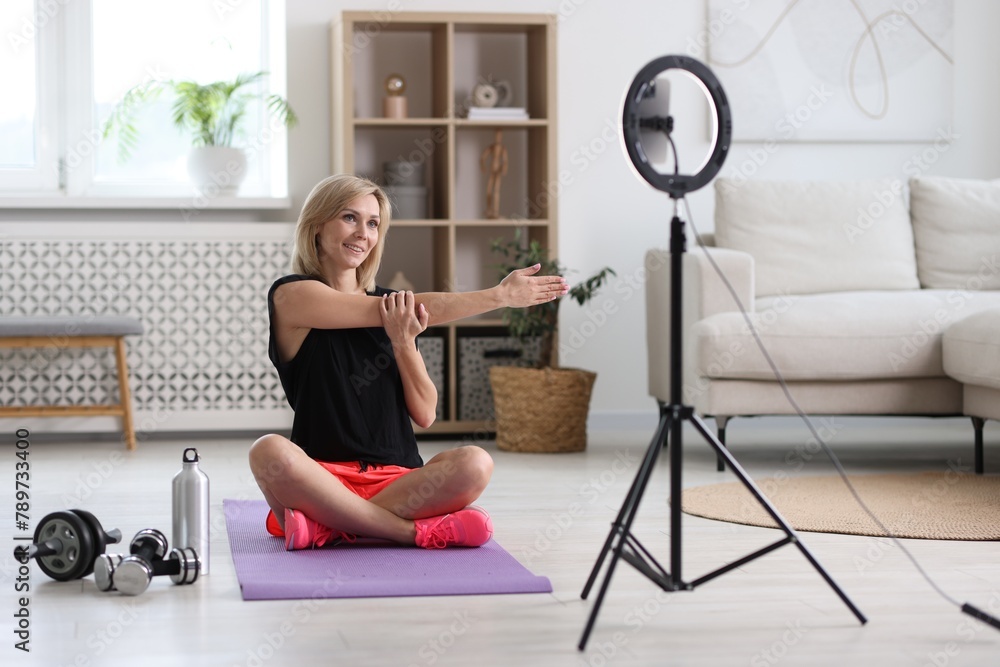 Smiling sports blogger streaming online fitness lesson with smartphone at home Smiling sports blogger streaming online fitness lesson with smartphone at home