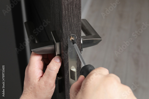 Handyman with screwdriver repairing door handle indoors, closeup