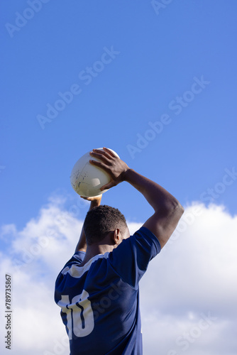 African American young male athlete holding a rugby ball, ready to throw, copy space