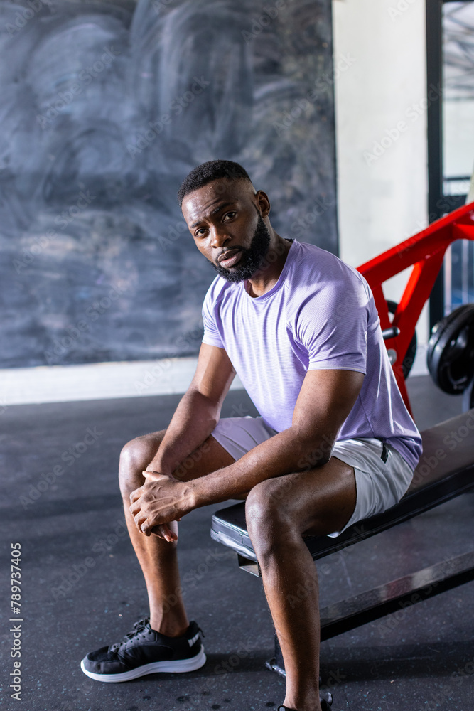 African American young male athlete sitting on a bench in a gym, copy space