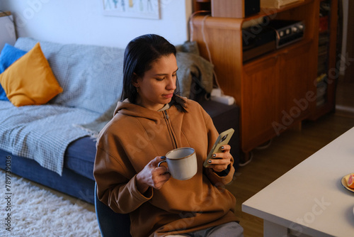 Woman checking smartphone at home while having coffee photo