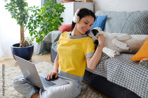 Woman with headphones at home using laptop while bonding with dog  photo