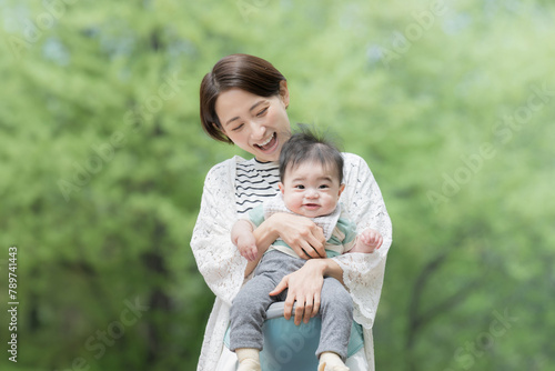 A mother (mother) holding her baby in a fresh green park Image of bright childcare, child rearing, and lifestyle © kapinon