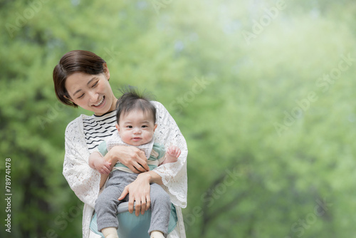 新緑の公園で赤ちゃんを抱っこするママ(母親)　明るい育児や子育て、ライフスタイルのイメージ © kapinon