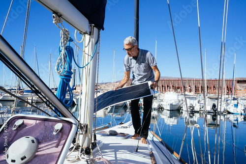 Mature man on sailboat carrying solar panel photo