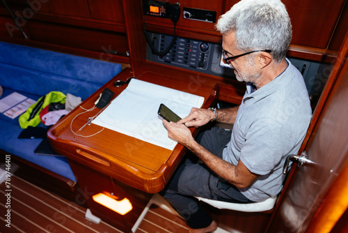 Middle age man browsing smartphone while sitting at table in yacht
