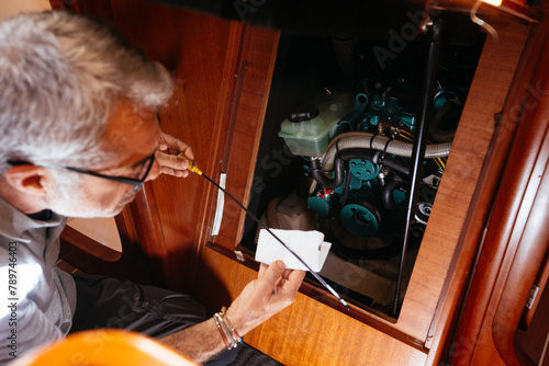 Senior mechanic checking oil level of engine on yacht with dipstick photo