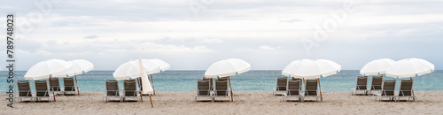panorama of a row of empty brown chairs and white umbrellas set up on a beach in the early morning,