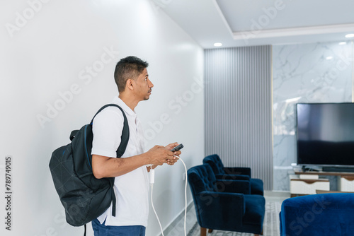 Positive slim man with bagpack and smartphone in light living room photo