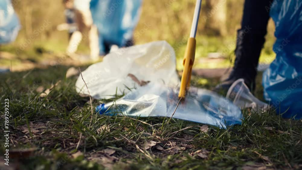 Group of volunteers cleaning the forest from litter and plastic waste, grabbing trash and junk with a long claw tool. Environmental activists picking up rubbish. Close up. Camera B. Group of volunteers cleaning the forest from litter and plastic waste, grabbing trash and junk with a long claw tool. Environmental activists picking up rubbish. Close up. Camera B.