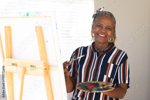 African American senior woman painting on canvas at home, wearing striped shirt photo