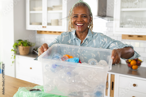 African American senior woman holding recycling bin in kitchen at home photo