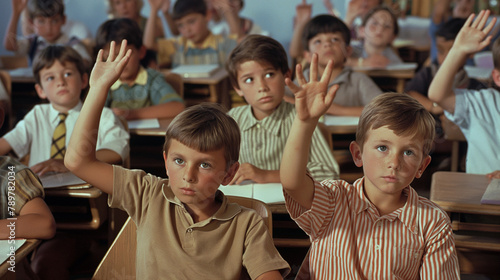 A group of children are sitting at their desks in a classroom raising their hands.

